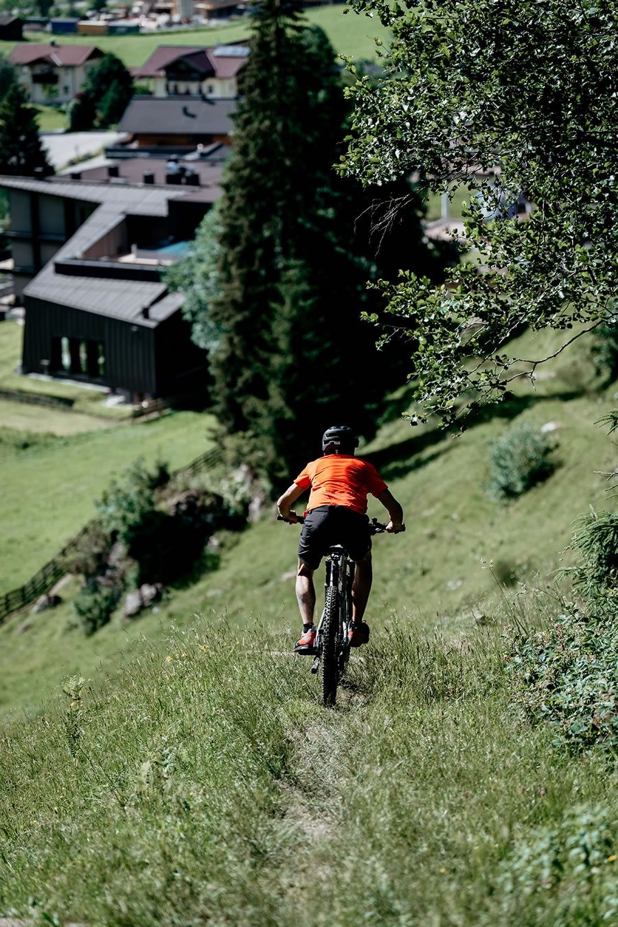 Ein Mountainbiker in rotem Trikot fährt einen grasbewachsenen Hügel zu Schernthaner sports in Kleinarl hinunter