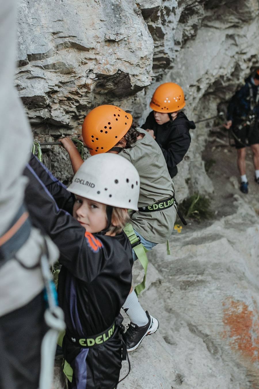 Kinder in Kletterausrüstung erklimmen eine steinige Felswand im Klettersteig in Kleinarl