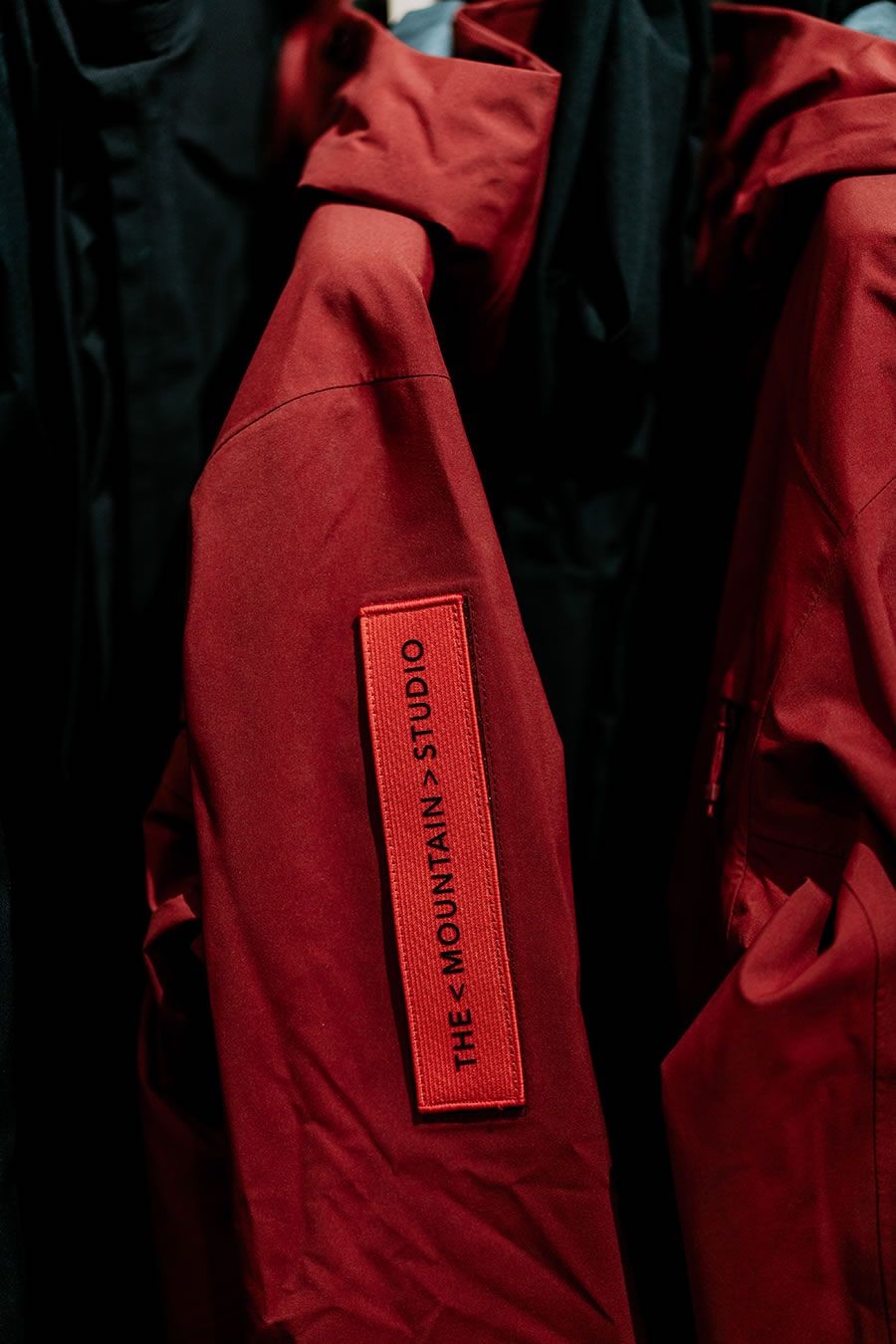 Rote Jacke mit schwarzem Schriftzug "THE MOUNTAIN STUDIO" auf dem Ärmel