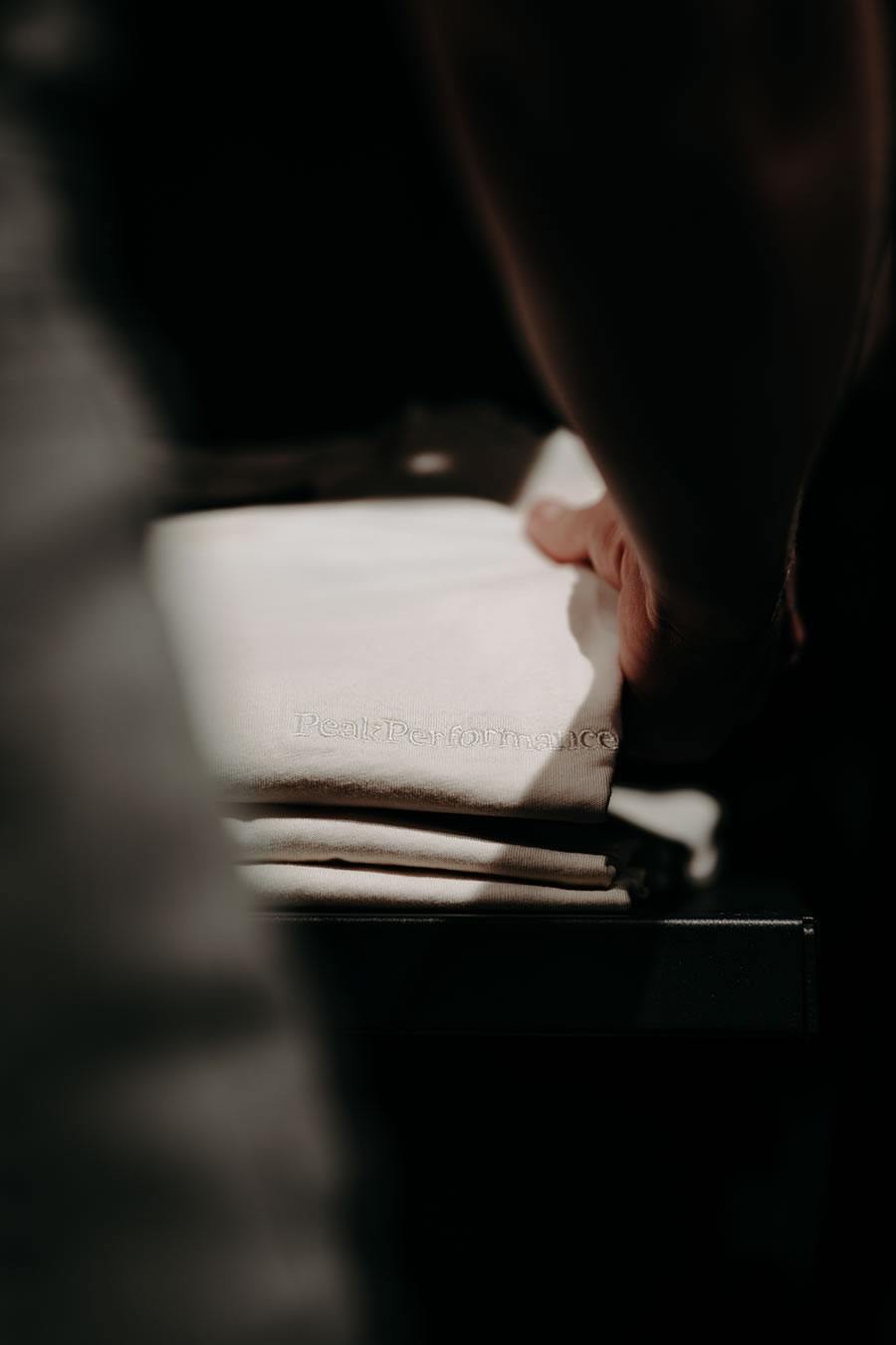 Eine Hand berührt ein gefaltetes, helles T-Shirt mit der Aufschrift "Peak Performance"