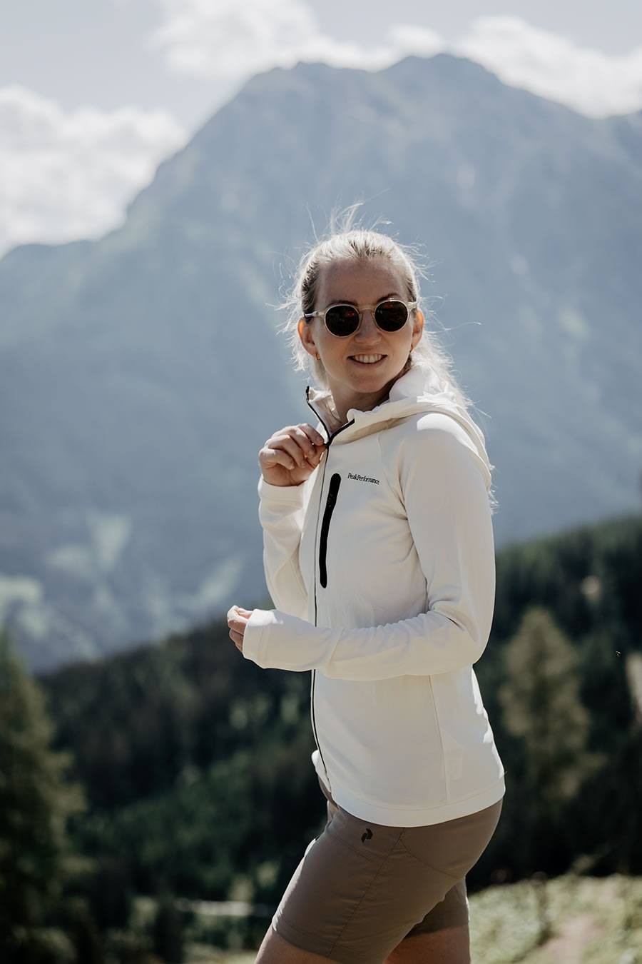 Frau in weißer Jacke und Sonnenbrille vor einer Berglandschaft