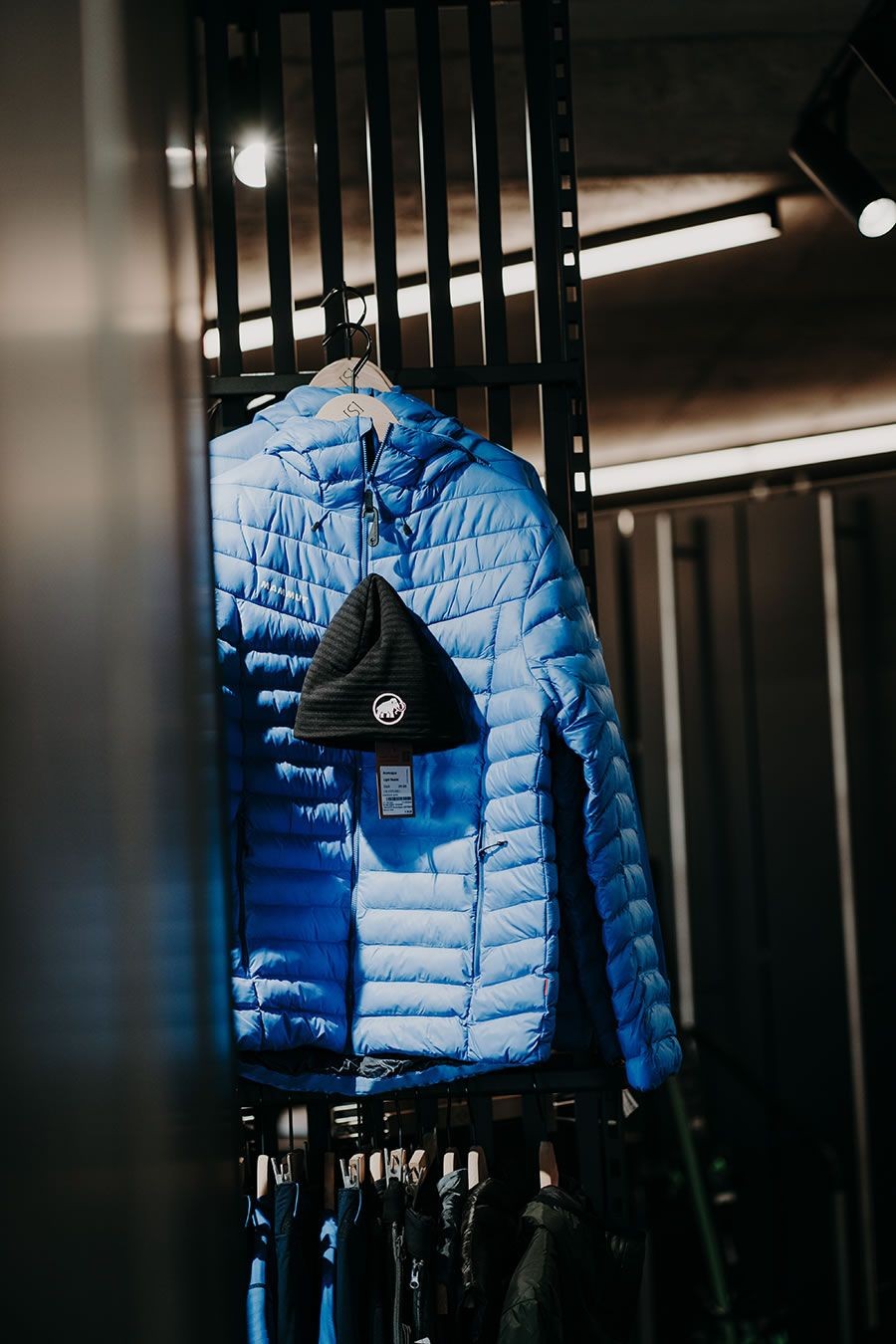 Blaue Daunenjacke und schwarze Mütze hängen an einem schwarzen Gitterständer