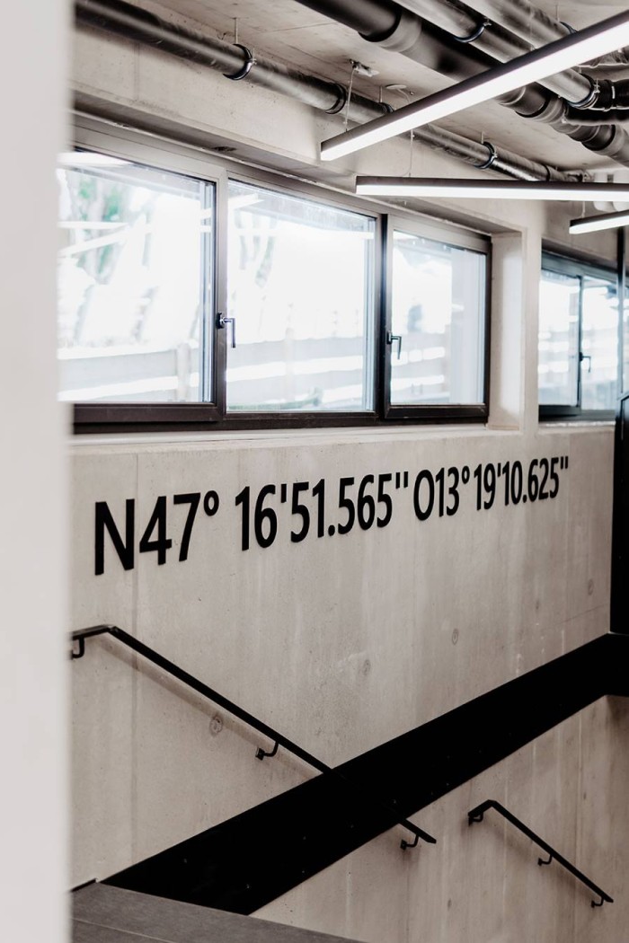 Koordinaten sind an einer Betonwand in einem modern gestalteten Treppenhaus zu sehen