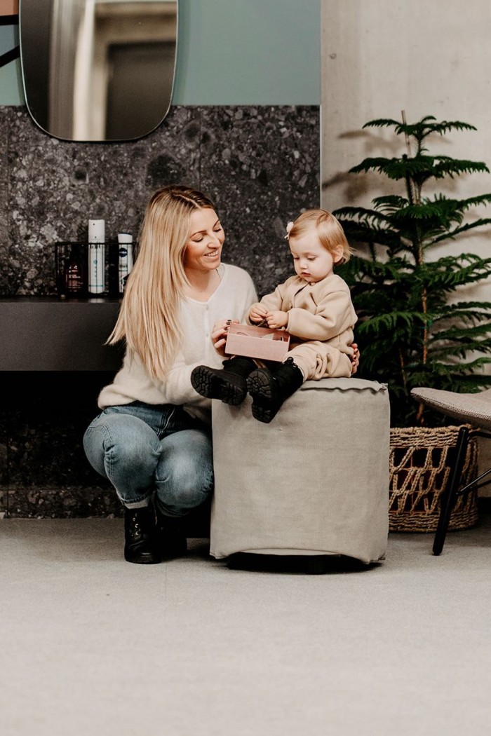 Frau kniet neben Kind auf Hocker, beide halten Geschenk und lächeln