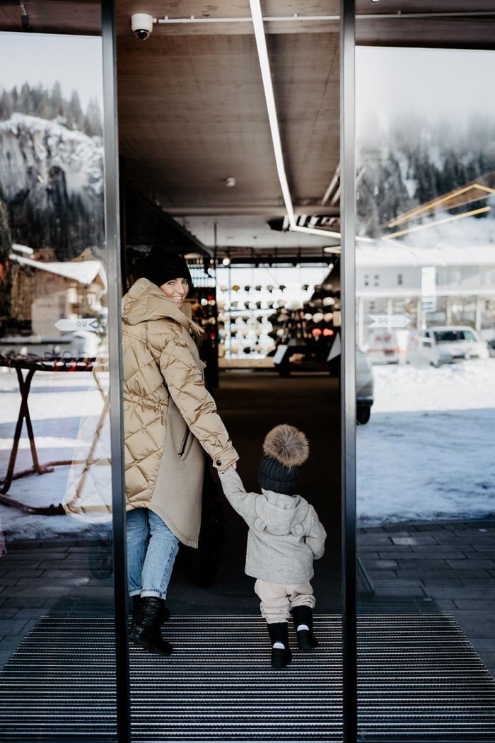 Eine lächelnde Person betritt mit einem Kind ein Gebäude in winterlicher Umgebung