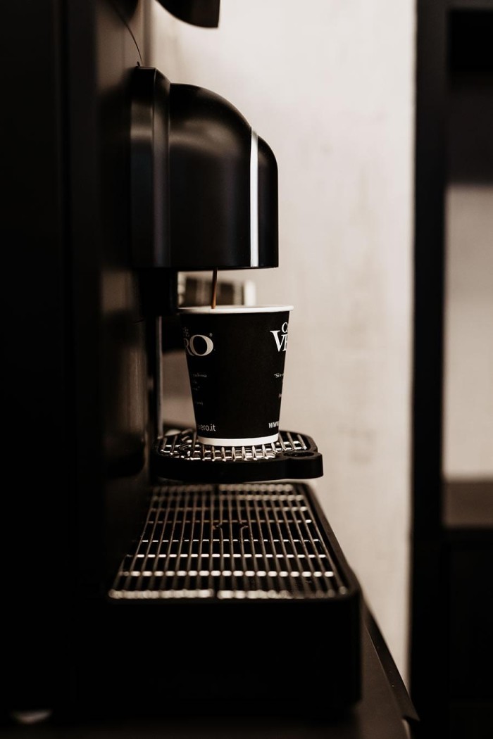 Ein schwarzer Kaffeeautomat brüht Kaffee in einen Pappbecher