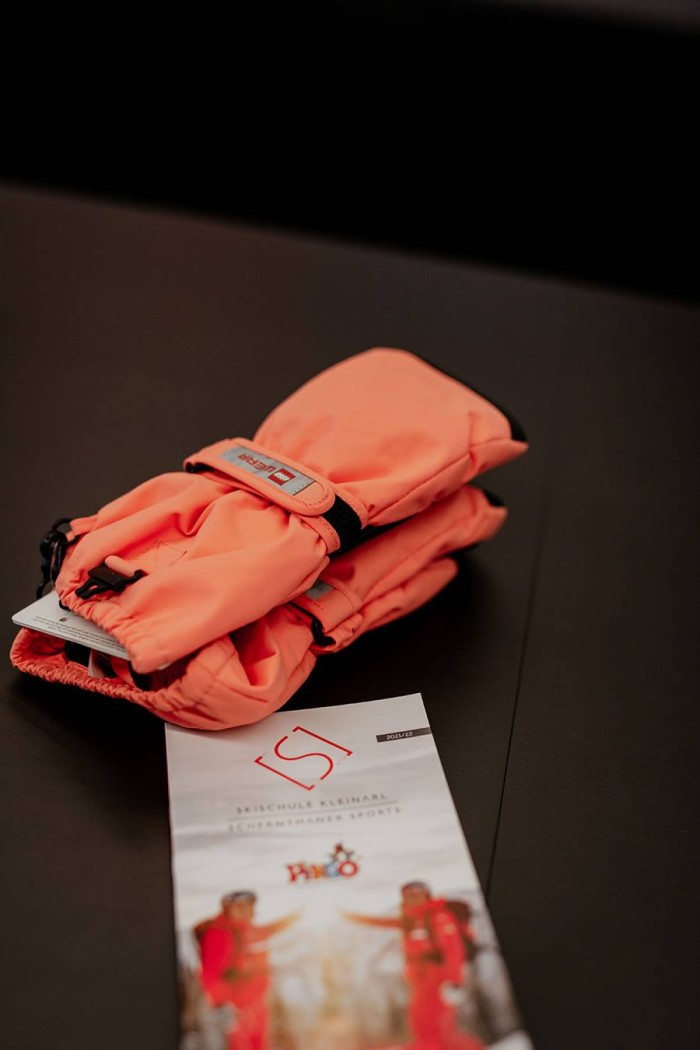 Orange Skihandschuhe liegen auf einem Tisch neben einem Prospekt