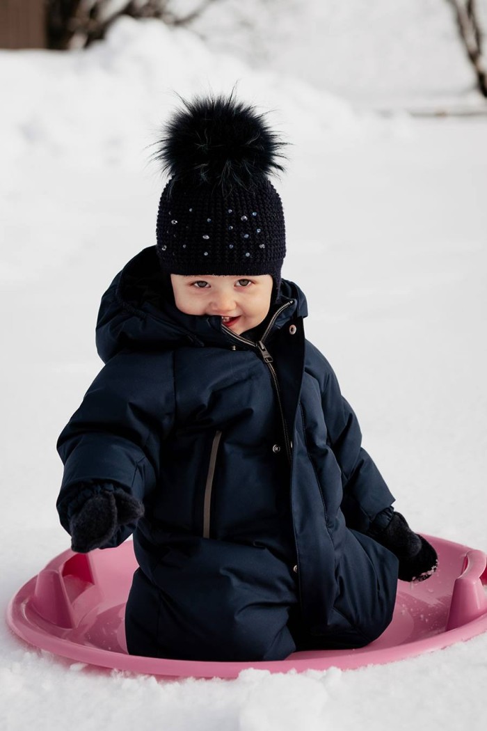Kleinkind in warmer Kleidung sitzt fröhlich auf einem pinken Schlitten im Schnee