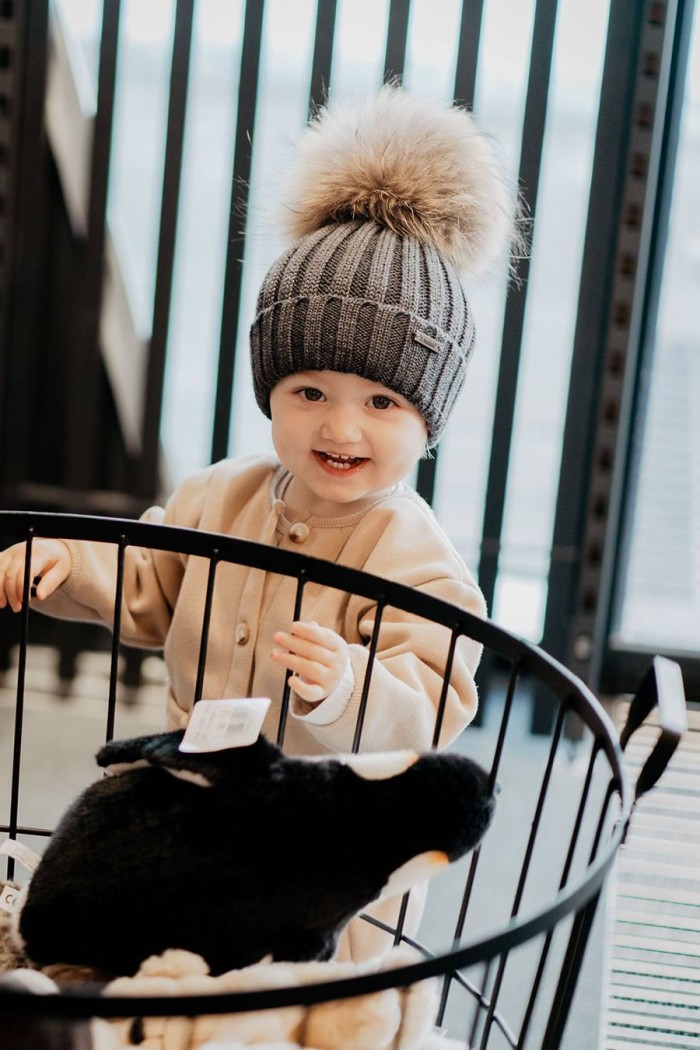 Ein lächelndes Kind mit grauer Mütze steht hinter einem Gitterkorb mit Plüschtier