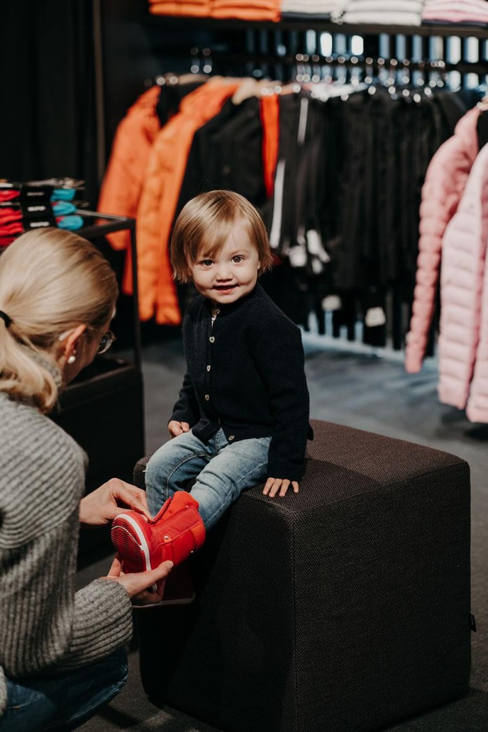 Ein Kind sitzt in einem Geschäft, während eine Person ihm rote Schuhe anzieht