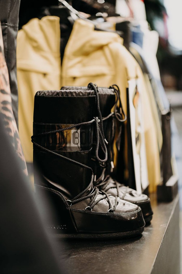 Schwarze Stiefel mit Schnürsenkeln stehen vor gelben Jacken auf einem Regal