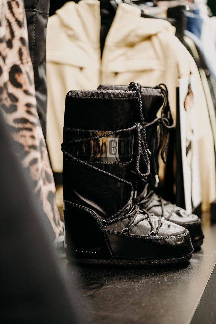 Schwarze Schnee-Stiefel mit Schnürsenkeln stehen auf einem Tisch vor beiger Kleidung