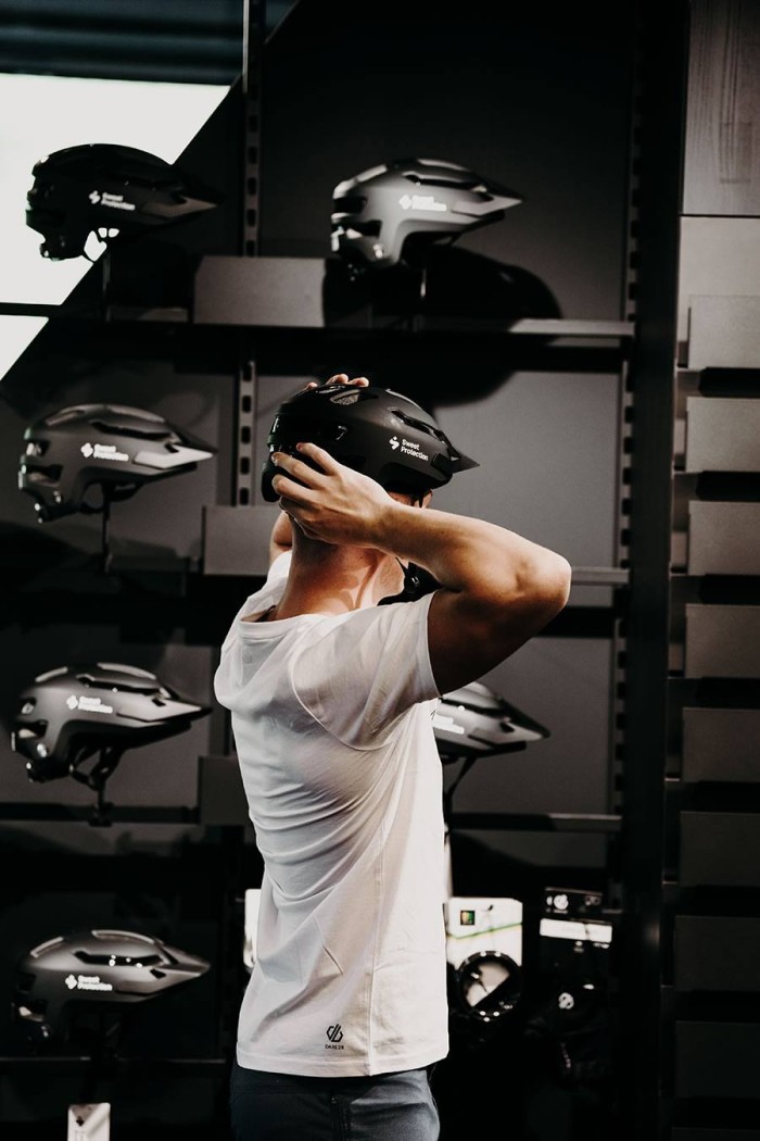 Person probiert einen schwarzen Helm in einem Laden an, umgeben von weiteren Helmen