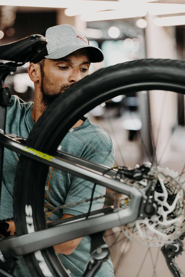 Ein Mann mit grauer Kappe inspiziert ein Fahrrad im Hintergrund