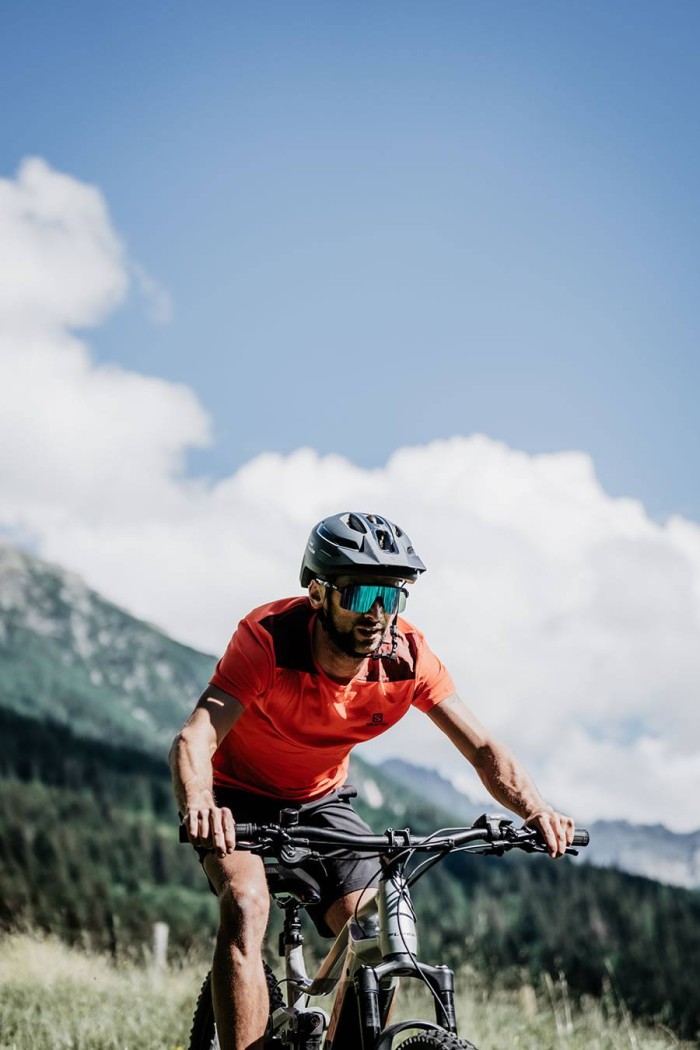 Mann in rotem Shirt fährt mit Fahrrad durch bergige Landschaft unter blauem Himmel