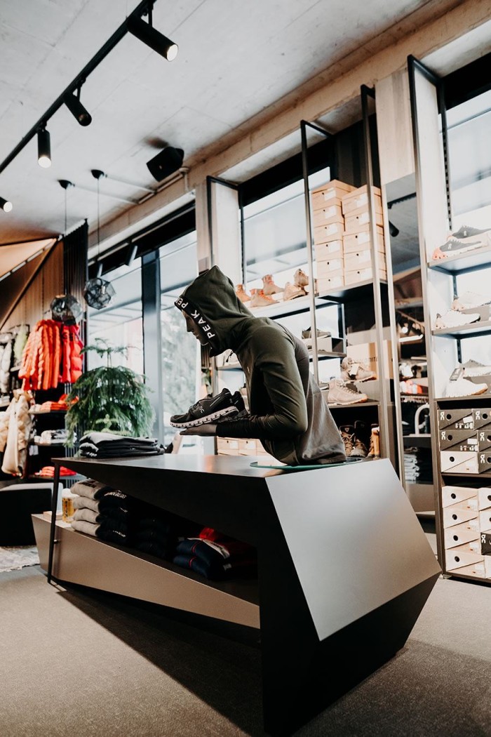 Person in grünem Hoodie hält Schuh in modernem Bekleidungsgeschäft