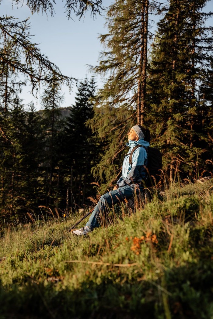 Eine Person sitzt entspannt auf einem Hang im Wald, beleuchtet vom Sonnenlicht