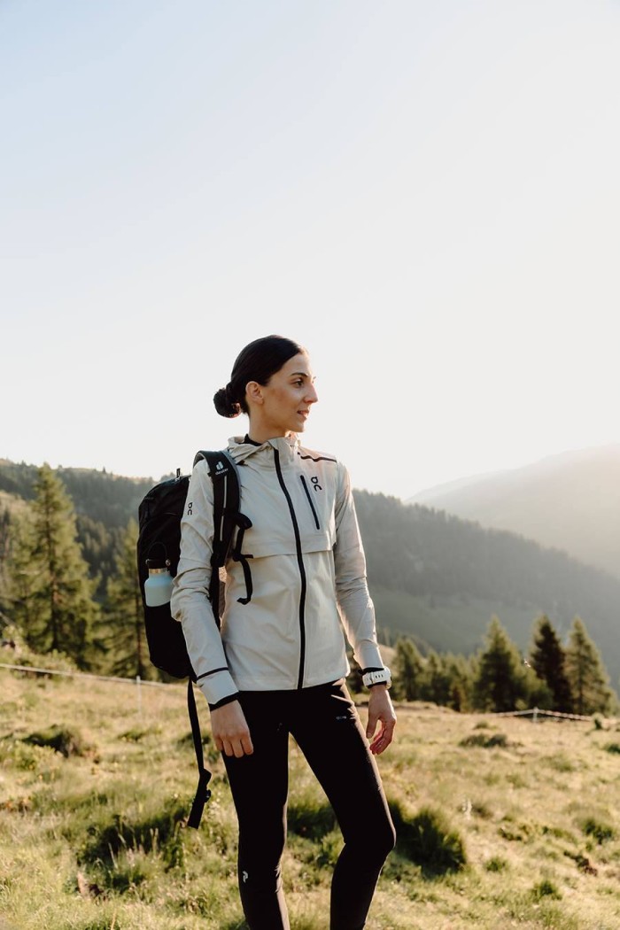 Person wandert mit Rucksack auf einer Wiese mit Bergblick im Hintergrund