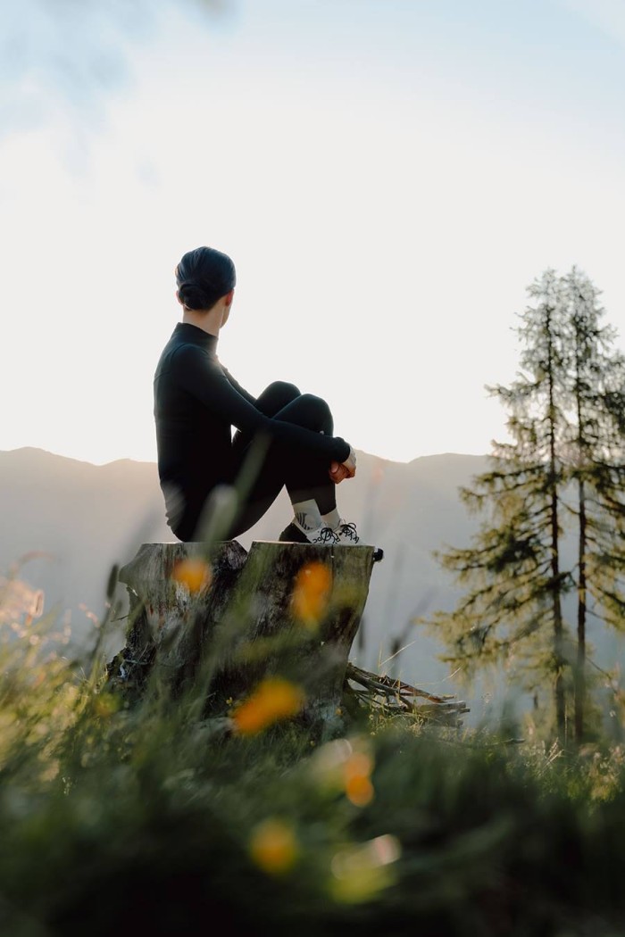 Eine Person sitzt auf einem Baumstumpf und blickt in die Berglandschaft