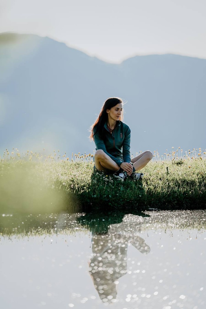 Frau sitzt in der Natur am Wasser, ihre Spiegelung ist sichtbar