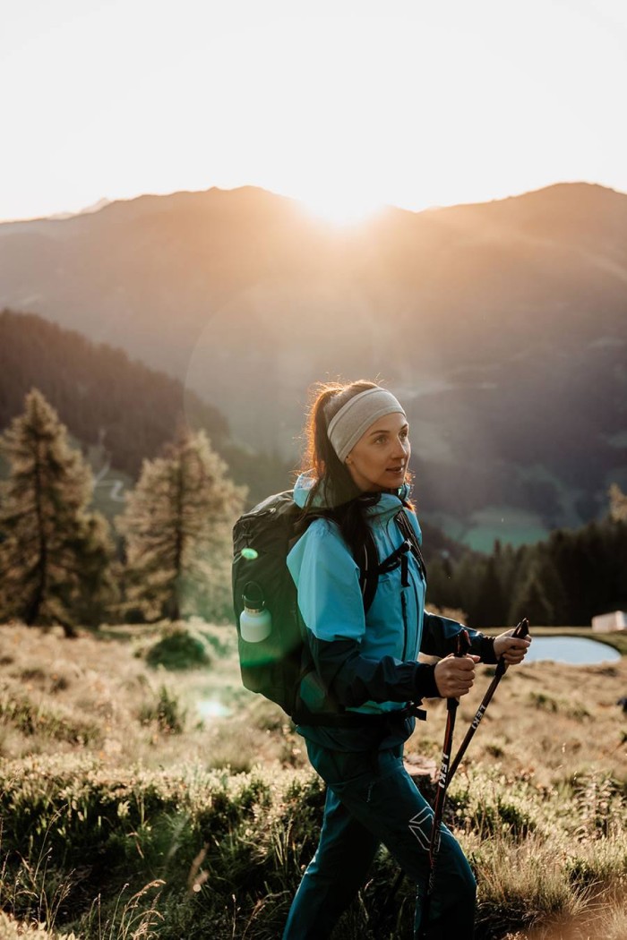 Frau wandert mit Stöcken in den Bergen bei Sonnenuntergang
