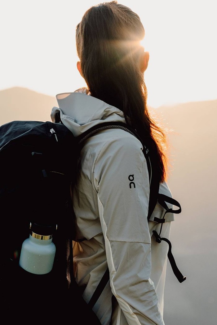 Eine Person in Outdoor-Kleidung blickt mit einem Rucksack in die Sonne
