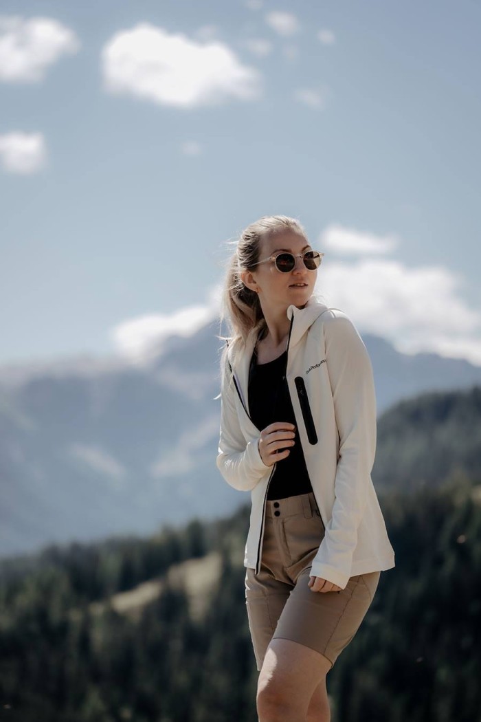 Eine Frau mit Sonnenbrille steht vor einer Berglandschaft
