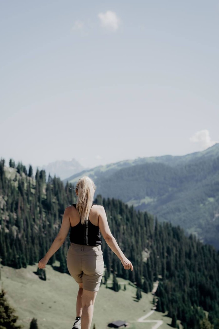 Eine Frau wandert auf einem Bergpfad mit Blick auf bewaldete Hügel und blauen Himmel