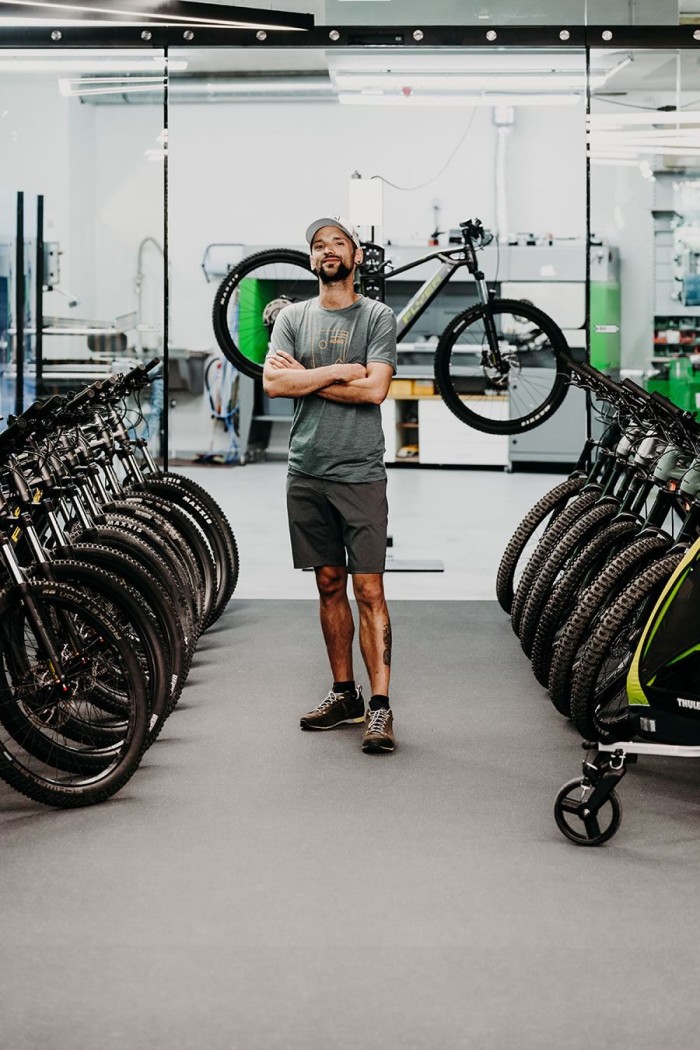 Mann steht in einer Fahrradwerkstatt zwischen zwei Reihen aufgestellter Fahrräder