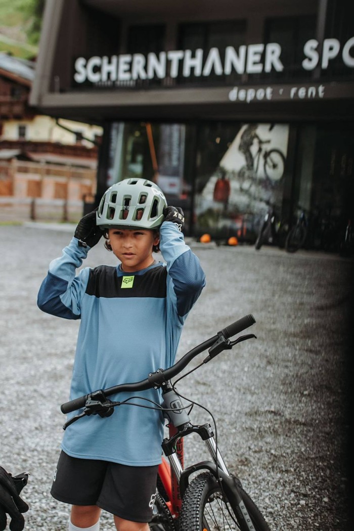 Ein Kind mit Fahrradhelm steht neben einem Fahrrad vor einem Sportgeschäft