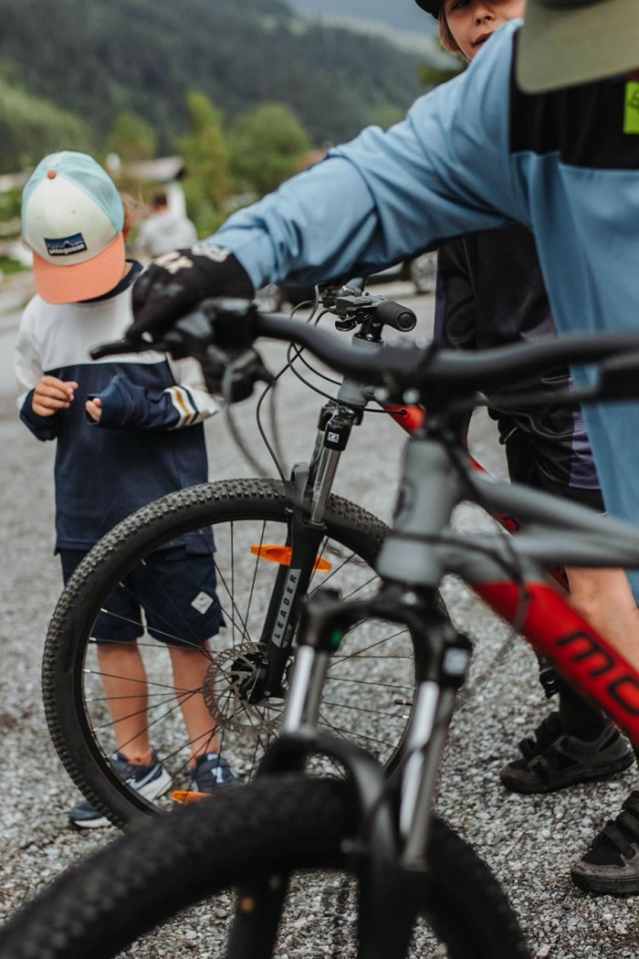 Zwei Personen mit Mountainbikes stehen auf einem Kiesweg, im Hintergrund ein Kind mit Mütze