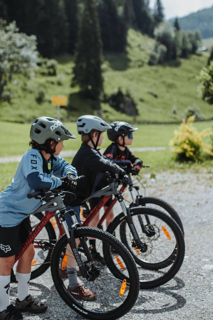 Drei Kinder mit Helmen fahren Fahrräder in einer grünen Landschaft