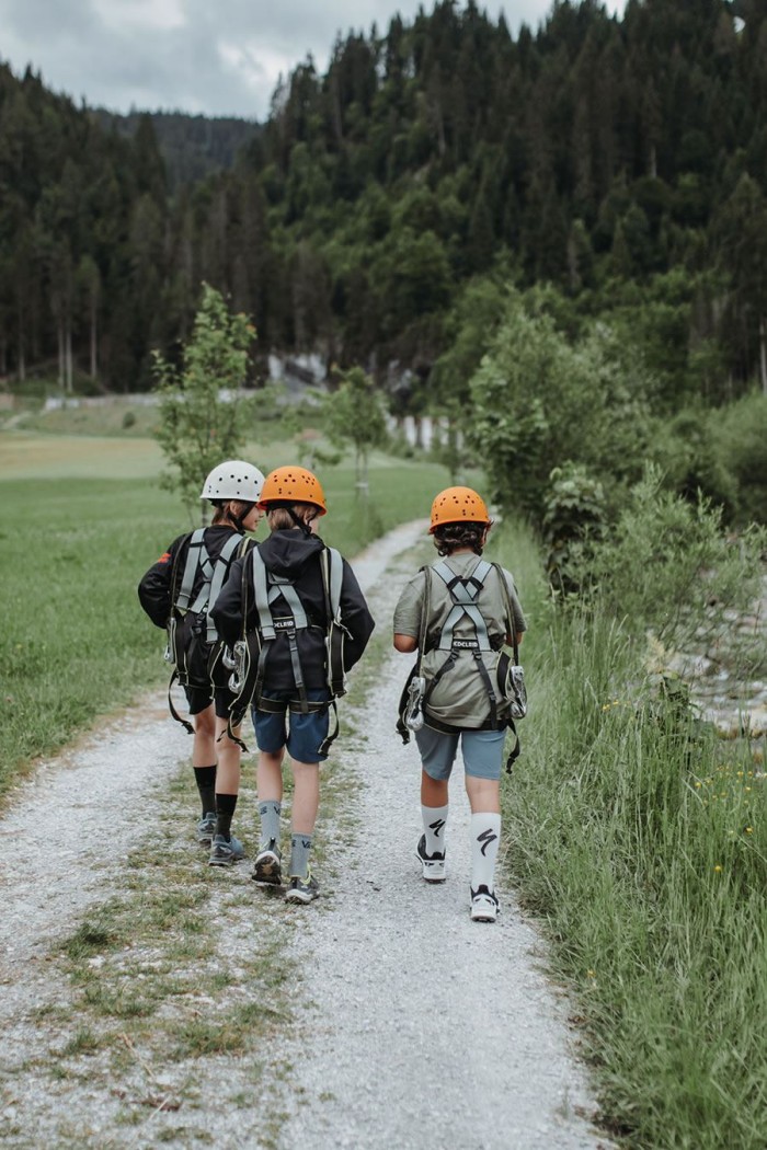 Drei Kinder mit Kletterausrüstung gehen einen Waldweg entlang