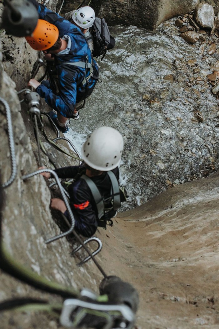 Drei Personen klettern mit Kletterausrüstung eine felsige Schlucht hinauf