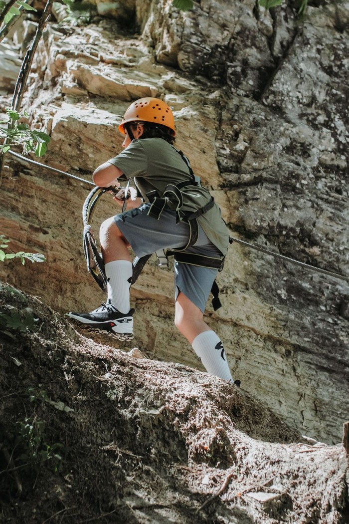 Eine Person klettert mit Helm und Seil eine felsige Wand hinauf
