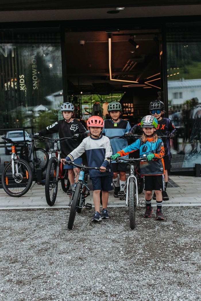Kinder in Fahrradhelmen stehen mit Mountainbikes vor einem Geschäft