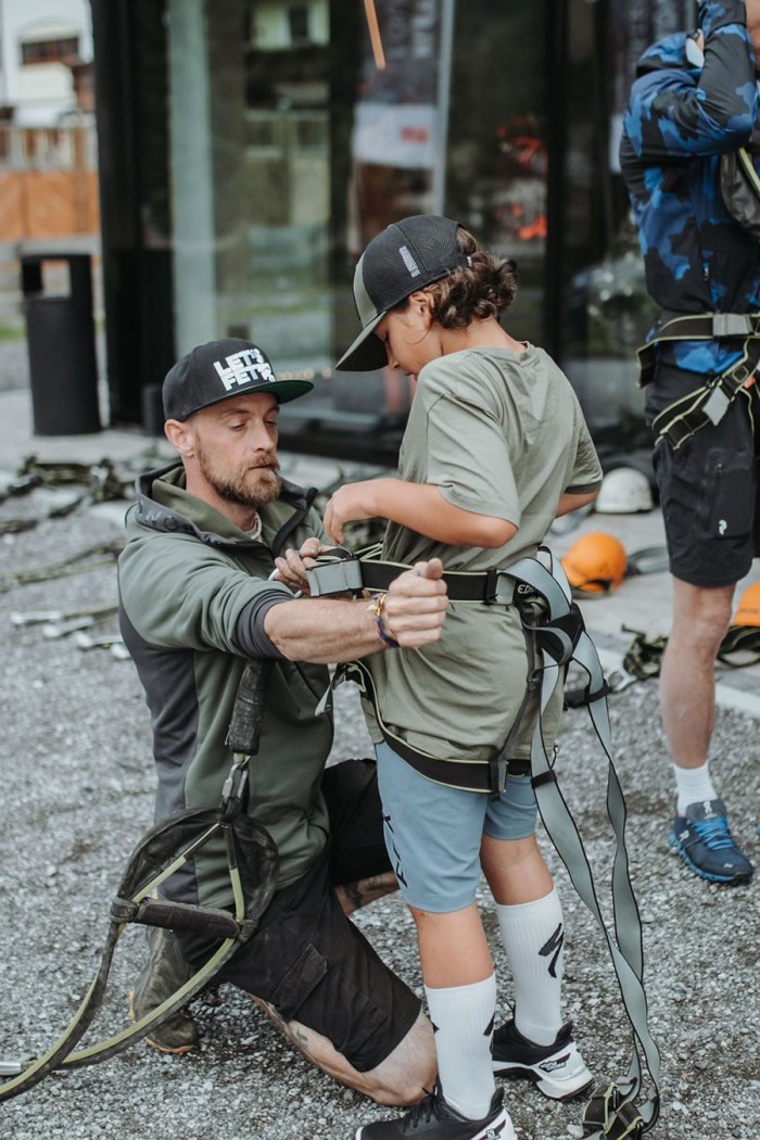 Erwachsener hilft Kind beim Anziehen eines Klettergurts im Freien