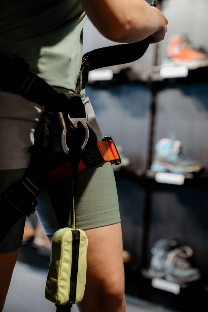 Person mit Klettergurt, vor einem Regal mit Schuhen stehend