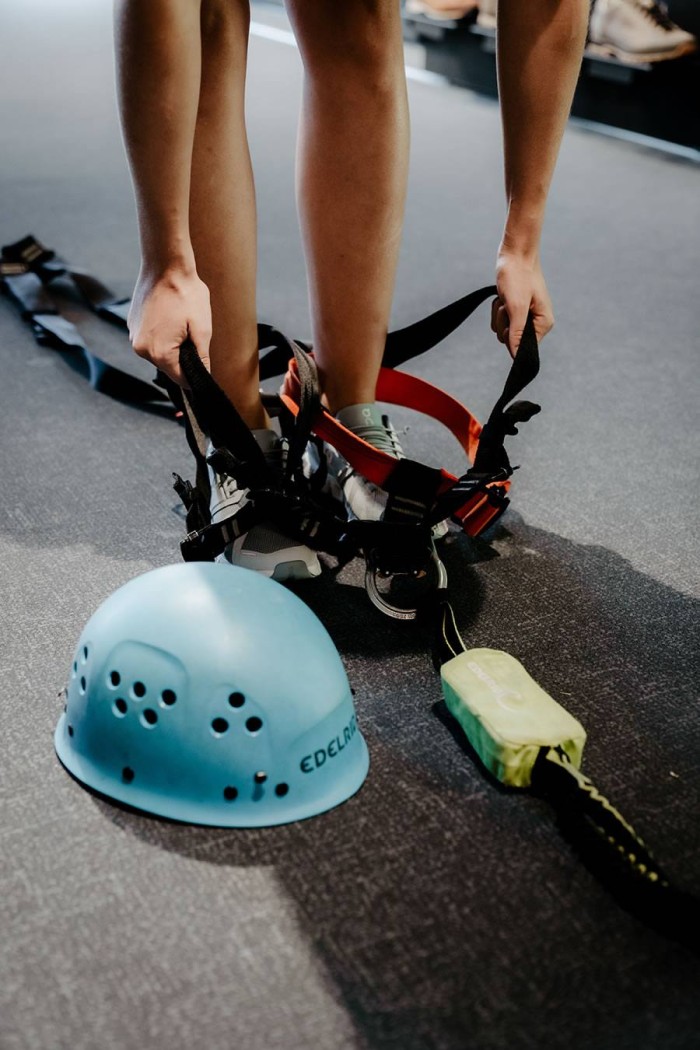 Person zieht Klettergurt an, blauer Helm liegt auf dem Boden