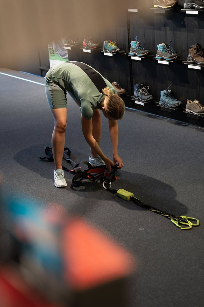 Person in Sportkleidung überprüft Kletterausrüstung in einem Laden mit Wanderschuhen