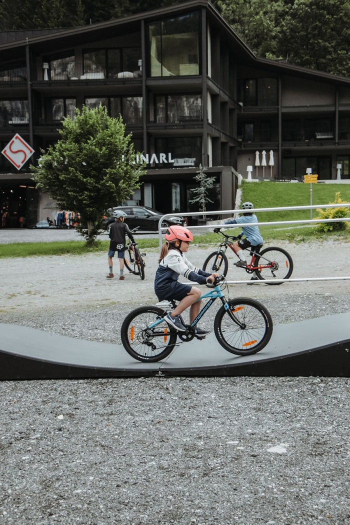 Kind fährt mit einem blauen Fahrrad über einen gewellten Fahrradparcours vor einem Gebäude