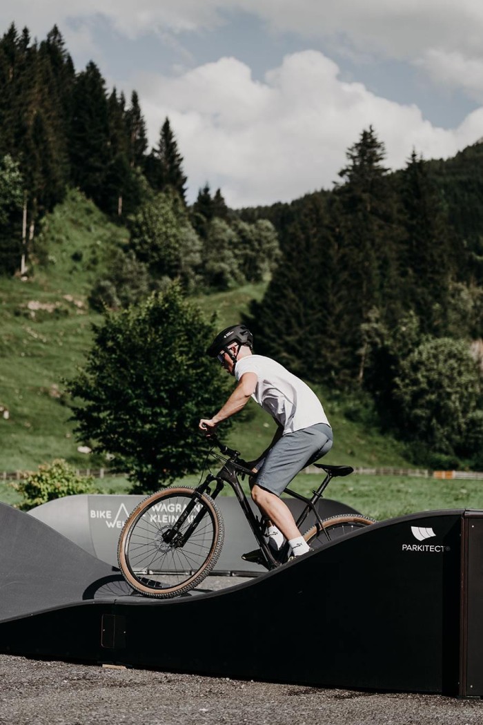 Ein Mensch fährt mit einem Fahrrad über eine Rampe in einer grünen Landschaft