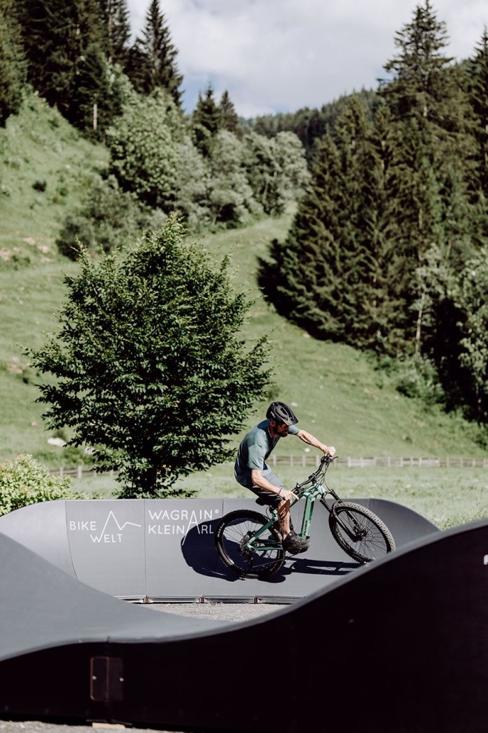 Ein Mountainbiker fährt auf einem Pumptrack in einer grünen, bewaldeten Berglandschaft