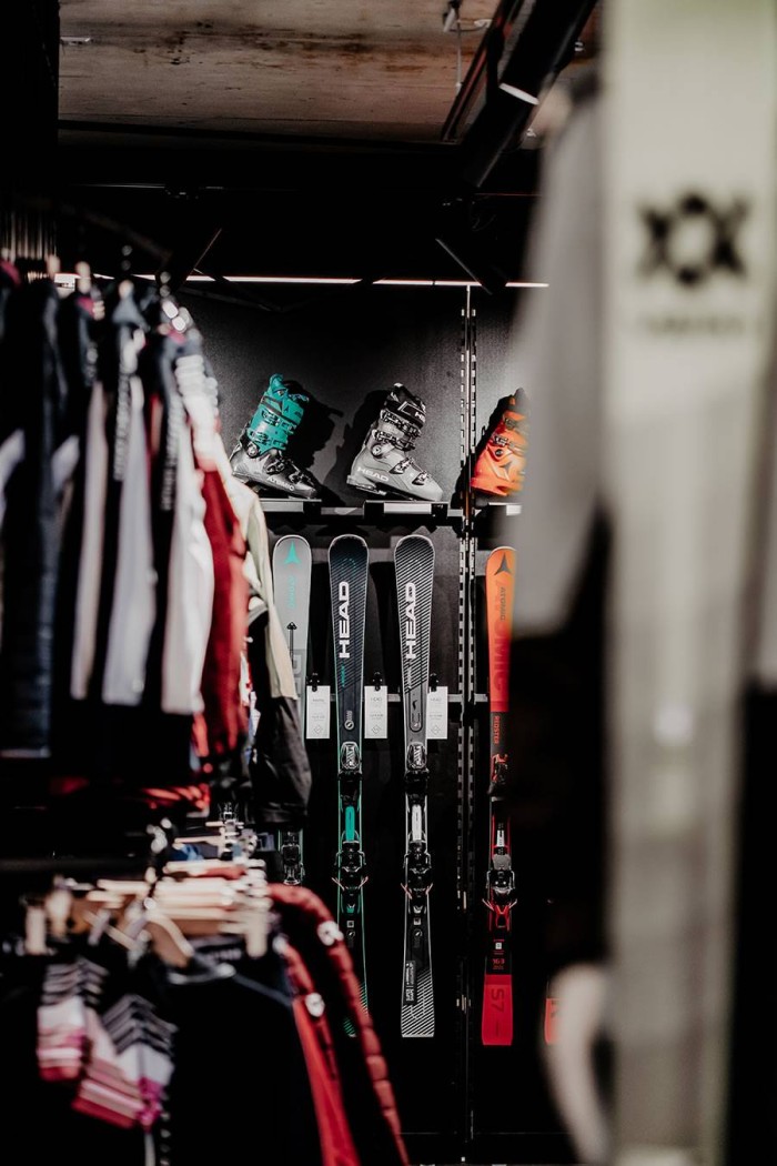 Skiausrüstung im Regal eines Sportgeschäfts, umgeben von Jacken und Kleidung