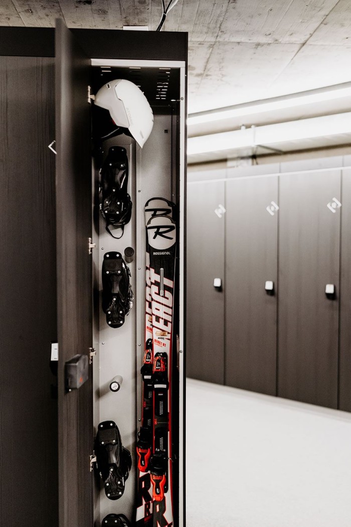Ein geöffneter Schrank im Skiraum zeigt Skier, Helm und Skischuhe