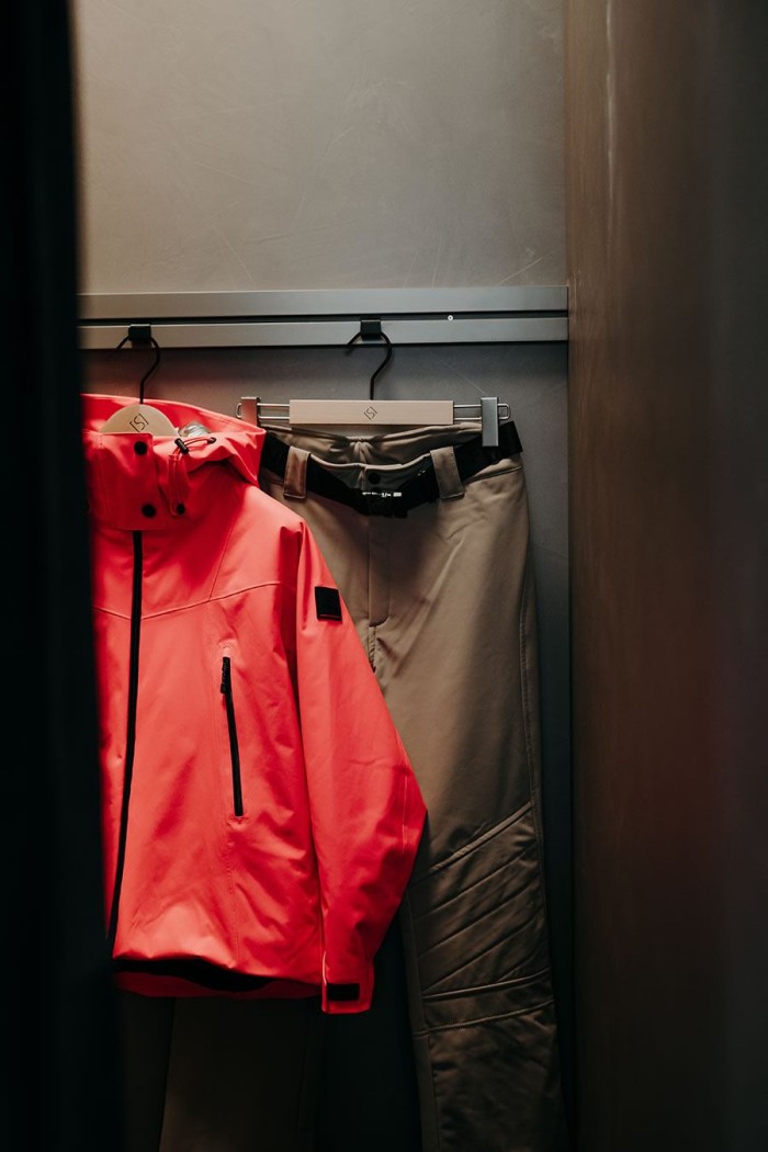 Rote Jacke und graue Hose hängen nebeneinander in einer Umkleidekabine