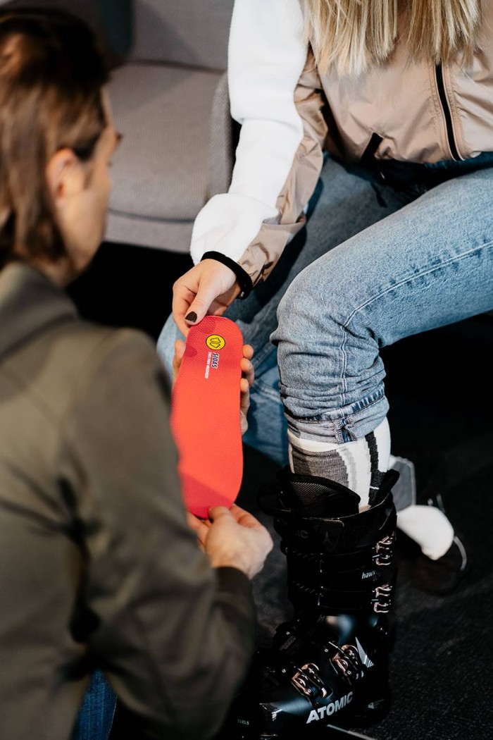 Eine Person legt eine rote Einlegesohle in einen schwarzen Skischuh ein