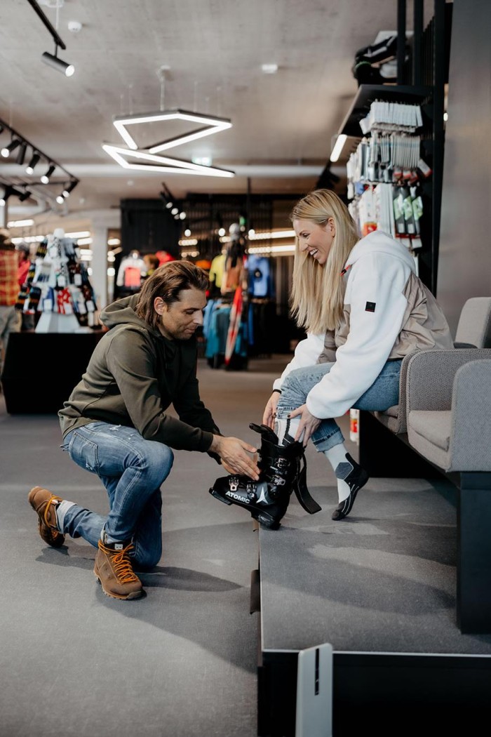Ein Mann hilft einer Frau, ihre Skischuhe in einem Sportgeschäft anzuziehen