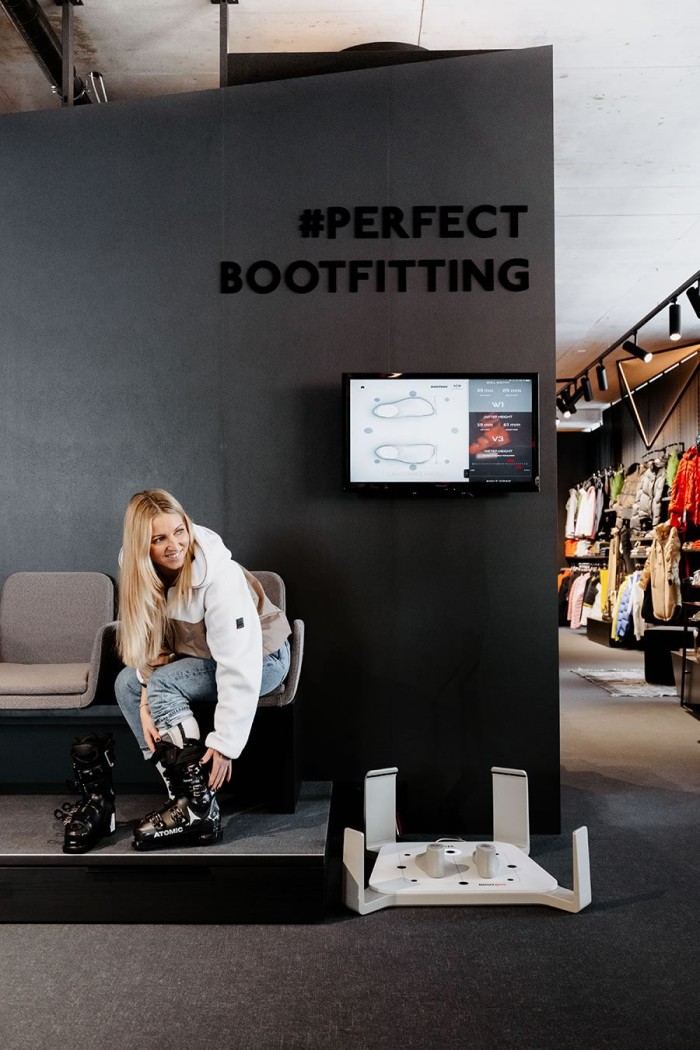 Eine Frau probiert Skischuhe an, während auf einem Bildschirm "Perfect Bootfitting" steht