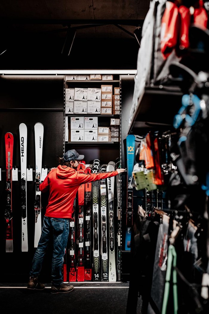 Ein Mann im roten Hoodie betrachtet Skiausrüstung in einem Geschäft